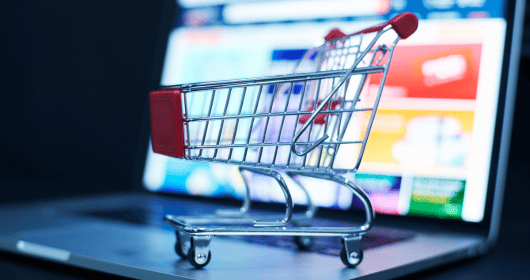 Small shopping cart in front of a laptop screen displaying an online store.